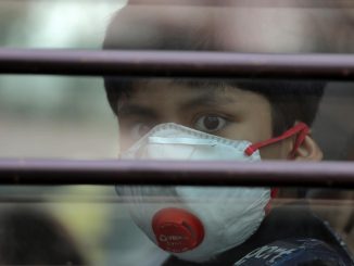 A schoolboy wearing a protective mask looks on from the inside of a school bus at Silver Line Prestige School in Ghaziabad